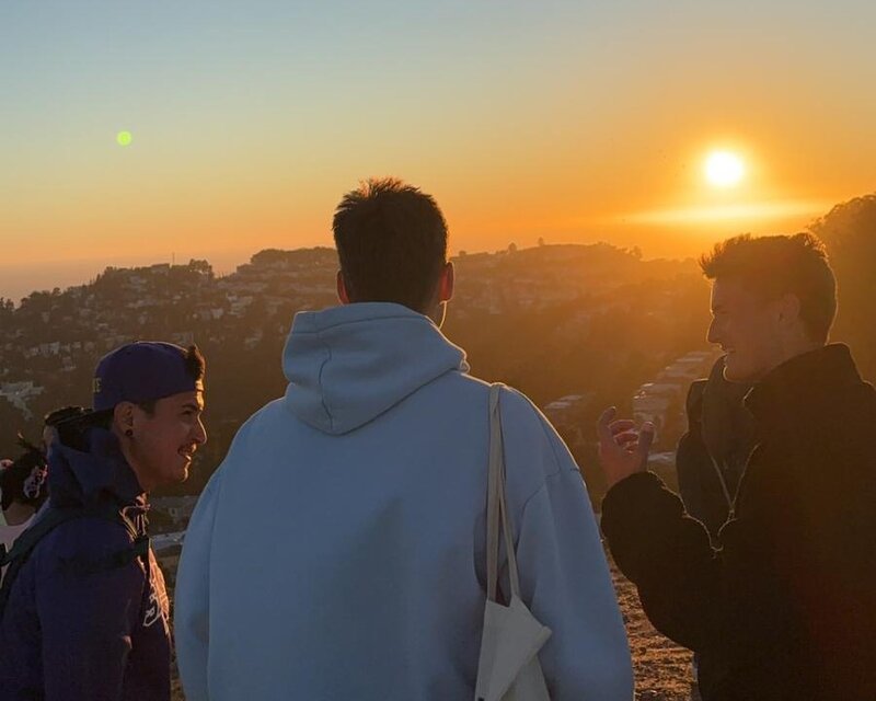 Drei Studierende genießen den Sonnenuntergang auf den Twin Peaks in San Francisco, mit Blick auf die Stadt und umliegende Hügel.