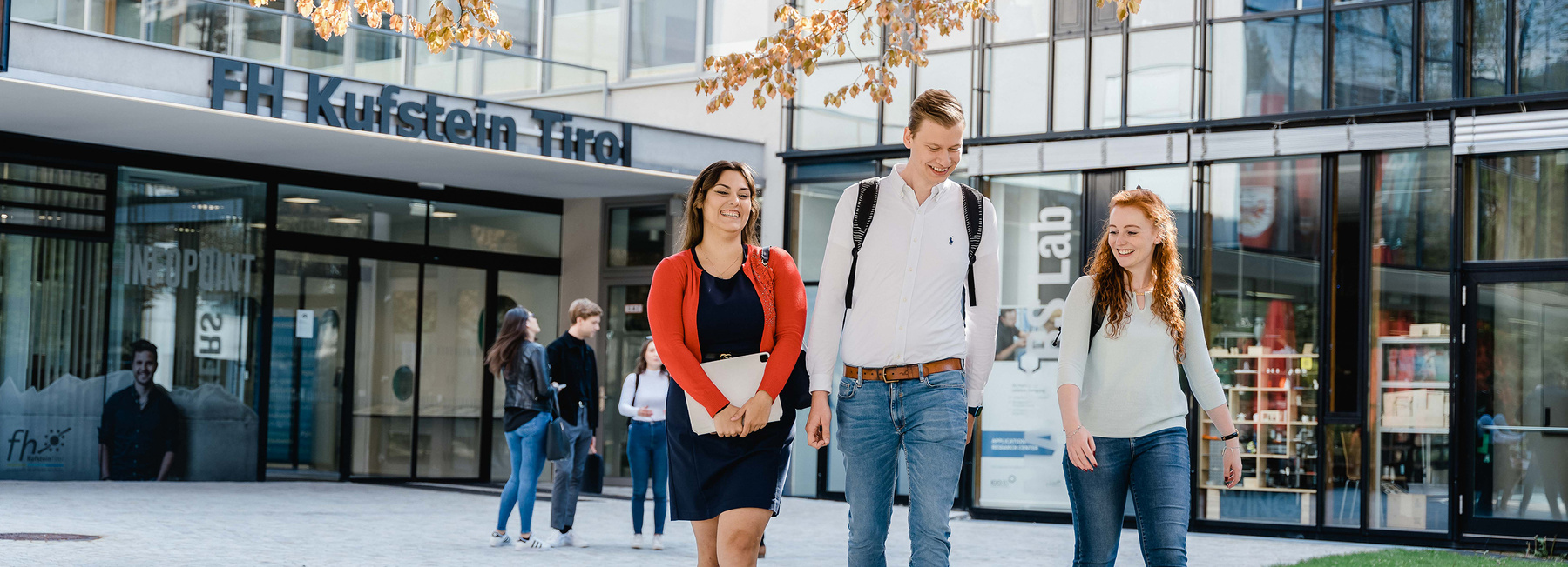 Drei Studierende der FH Kufstein Tirol gehen über den Campus vor dem Haupteingang der Hochschule.
