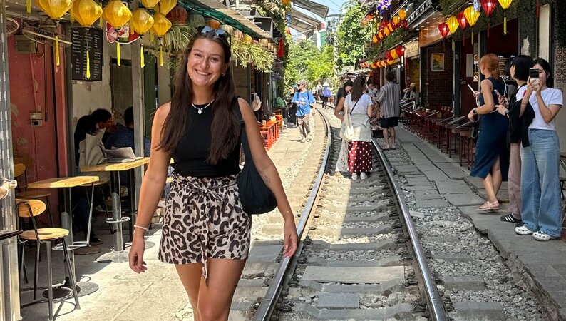 Magdalena Bernrieder in einer geschäftigen Einkaufsstraße in Malaysia, umgeben von lokalen Geschäften und Passant:innen.